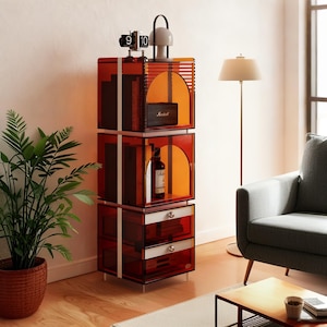 Puede incluir: Un moderno mueble de almacenamiento de tres niveles con un tono rojo-naranja transparente. El mueble presenta cortes arqueados, detalles blancos y cajones. Está coronado con un reloj retro y una pequeña lámpara. El mueble está en un salón.