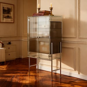 以下が含まれることがあります： シルバーの金属フレームと脚が付いたガラスのディスプレイキャビネット。 キャビネットには2つのガラスドアと内部の棚があります。 2つの真鍮の燭台にはろうそくが灯り、本が積まれています。