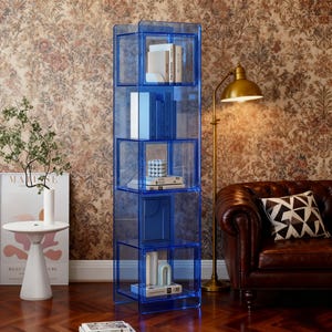 Puede incluir: Una estantería alta de acrílico azul transparente con múltiples cubículos. Los estantes contienen libros y objetos decorativos. La estantería está en una habitación con papel pintado floral y un sofá de cuero marrón.