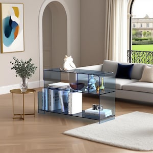 Puede incluir: Estantería moderna de cristal azul transparente con múltiples estantes. La unidad está llena de libros, objetos decorativos y una pequeña cámara. También se ve una mesa auxiliar dorada con un jarrón con vegetación y una pintura abstracta colorida.