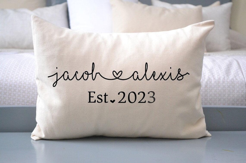 May include: A white pillow with black text that reads "jacob &hearts; alexis Est. 2023".