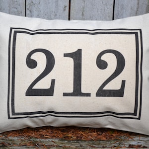 May include: A white pillow with a black border and the number 212 printed in black.