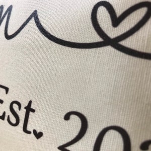 May include: White canvas pillow with black text that reads "Home Est. 202" and a black heart.