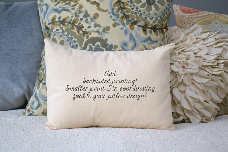 May include: A white pillow with the text "Add backsided printing! Smaller print & in coordinating font to your pillow design!" printed on it. The pillow is sitting on a white surface with other pillows behind it.