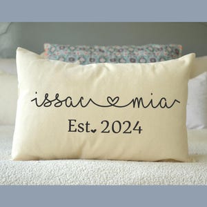 May include: A white throw pillow with the text "issac &hearts; mia" and "Est. 2024" in black cursive font.