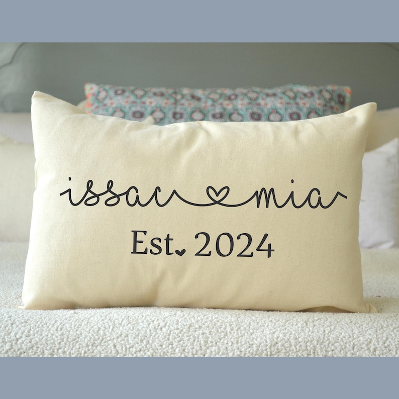 May include: A white throw pillow with the text "issac &hearts; mia" and "Est. 2024" in black cursive font.
