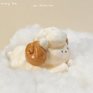 Pode incluir: Uma pequena figura de ovelha de cerâmica branca com chifres marrons, deitada sobre uma superfície branca e fofa. O texto "Summer for thee, grant may be --- From me" está escrito acima da ovelha.