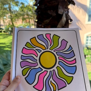 May include: A coloring book page with a colorful sun design. The sun is surrounded by a circle of wavy lines in shades of pink, purple, blue, green, and yellow.