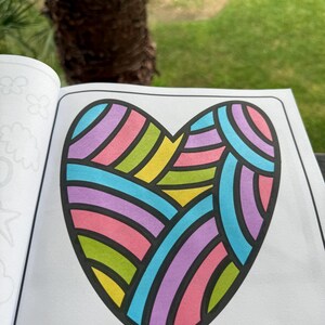May include: A coloring book page featuring a large heart shape with a colorful geometric pattern. The heart is outlined in black and filled with pink, purple, blue, green, and yellow stripes.