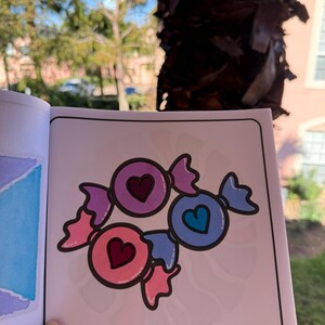 May include: A coloring page featuring three candy hearts with different colors and heart designs. The candy hearts are pink, purple, and blue.