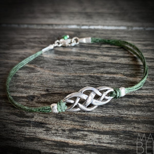 May include: A green cord bracelet with a silver Celtic knot charm. The bracelet is tied with a sliding knot for adjustability.