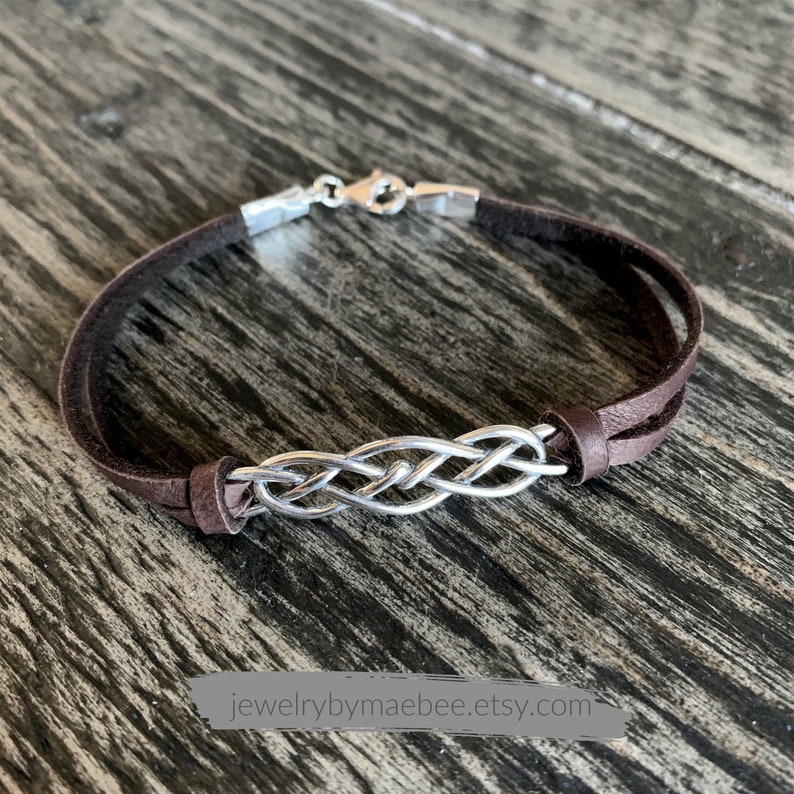 Puede incluir: Un brazalete de cuero marr&oacute;n con un dise&ntilde;o de nudo celta plateado. El brazalete tiene un cierre plateado.