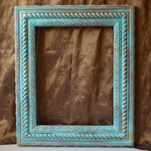 May include: A rectangular picture frame with a distressed turquoise finish and gold accents. The frame features a rope-like border and ornate detailing, creating a vintage aesthetic. The frame is empty, ready for a photo or artwork.