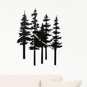 Peut inclure: Horloge murale noire représentant une silhouette de pins. Les aiguilles de l'horloge sont vert clair et le cadran est noir. L'horloge est fixée sur un mur blanc, avec un canapé blanc en dessous.
