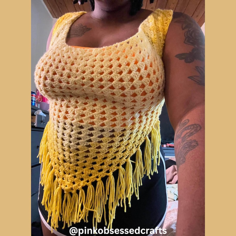 May include: A handmade, open-weave crochet top in shades of yellow, featuring a square neckline and fringe detail at the hem. The top is a sleeveless design, with a textured pattern and a bright, summery aesthetic. The text "@pinkobsessedcrafts" is visible at the bottom.