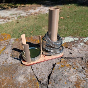 Op de afbeelding: Een handgemaakte ringwerpspelset. De set bevat een houten basis met een centrale cilinder en meerdere metalen ringen. De basis heeft ook twee kleine bakjes met deksels. De basis is beschilderd met een rode rand en een bladerontwerp.