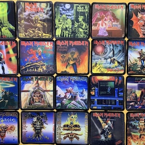 Puede incluir: Una colección de parches cuadrados de Iron Maiden, cada uno con arte de álbum. Los parches muestran varios diseños, incluyendo figuras, paisajes y el logotipo de la banda. Los parches están sobre una superficie amarilla.