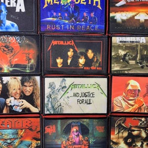 May include: A collection of twelve rectangular fabric patches featuring various heavy metal band album covers, including Pantera, Megadeth, Metallica, Sepultura, and Death, with visible band logos and album titles printed on each individual patch.