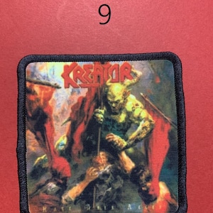 Peut inclure: &Eacute;cusson carr&eacute; &agrave; bordure noire avec le nom du groupe "KREATOR" en lettres rouges. L'&eacute;cusson repr&eacute;sente une sc&egrave;ne de bataille avec un monstre vert tenant une lance et des drapeaux rouges. Le texte "HATE DAYS A" est visible.