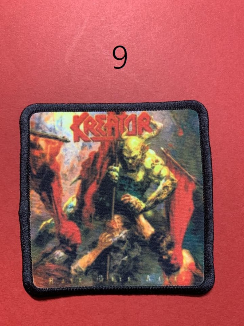 Peut inclure: &Eacute;cusson carr&eacute; &agrave; bordure noire avec le nom du groupe "KREATOR" en lettres rouges. L'&eacute;cusson repr&eacute;sente une sc&egrave;ne de bataille avec un monstre vert tenant une lance et des drapeaux rouges. Le texte "HATE DAYS A" est visible.