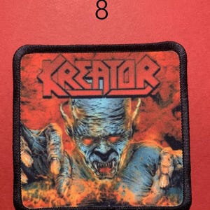 Peut inclure: &Eacute;cusson carr&eacute; avec le mot "KREATOR" en lettres rouges au-dessus d'une figure d&eacute;moniaque aux yeux rouges et aux mains tendues. Le fond est orange et rouge flamboyant. L'&eacute;cusson a une bordure noire et le chiffre "8" est au-dessus.