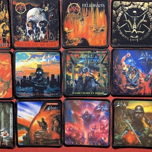May include: A collection of square patches featuring album art from various heavy metal bands. The patches display vibrant, detailed illustrations with themes of skulls, demons, and apocalyptic scenes. The patches are in various colors, including red, orange, and black.