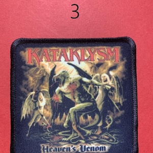 Peut inclure: &Eacute;cusson carr&eacute; avec le mot "KATAKLYSM" en rouge, au-dessus d'une illustration de personnages ail&eacute;s et des mots "Heaven's Venom". L'&eacute;cusson a une bordure noire et est sur un fond rouge. Le chiffre "3" est au-dessus de l'&eacute;cusson.