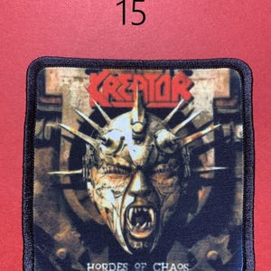Peut inclure: &Eacute;cusson carr&eacute; &agrave; bordure noire avec le nom du groupe "KREATOR" en rouge et une illustration d'un visage hurlant avec des pointes. Le texte "HORDES OF CHAOS" est en dessous de l'image. Le num&eacute;ro "15" est au-dessus de l'&eacute;cusson.