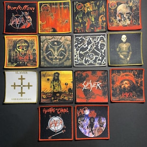 May include: A selection of square, embroidered patches with diverse designs and the band name "Slayer." The patches showcase images of skulls, figures, and text such as "Hell Awaits" and "God Hates Us All." The patches are in various colors, including black, red, and white.