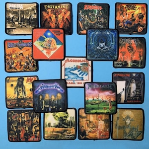 以下が含まれることがあります： 様々なヘヴィメタルバンドのアルバムアートワークが描かれた正方形のパッチのコレクション。 メタリカ、メガデス、パンテラなど、カラフルなイラストとバンドロゴが、水色の背景に表示されています。