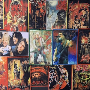 Puede incluir: Una colección de parches de la banda Slayer con arte de álbumes e imágenes de miembros de la banda. Los parches muestran varios colores, incluyendo rojo, negro y blanco, con el logotipo de la banda en un lugar destacado. Los parches son rectangulares y tienen un borde cosido.