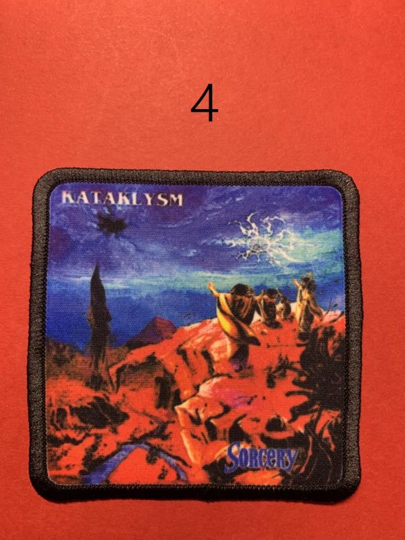 Peut inclure: &Eacute;cusson carr&eacute; &agrave; bordure noire repr&eacute;sentant un paysage fantastique avec des personnages sur une formation rocheuse rouge sous un ciel bleu. Le texte "KATAKLYSM" est en haut et "SORCERY" en bas.