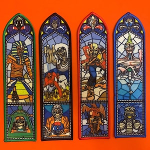 Peut inclure: Quatre écussons brodés rectangulaires à sommet arqué, chacun présentant un motif de vitrail illustrant diverses figures squelettiques. Les écussons ont des bordures verte, noire, rouge et bleue, et présentent des illustrations détaillées.