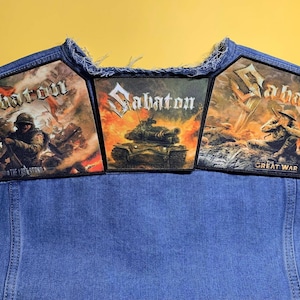 Könnte beinhalten: Eine blaue Jeansweste mit drei rechteckigen Aufnähern mit dem Sabaton-Logo. Der linke Aufnäher zeigt einen Soldaten im Kampf, der mittlere einen brennenden Panzer und der rechte einen Soldaten im Schützengraben mit dem Text The Great War.
