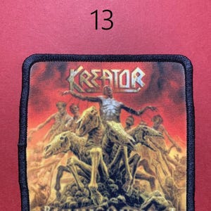 Peut inclure: Un &eacute;cusson carr&eacute; &agrave; bordure noire pr&eacute;sente le nom du groupe "KREATOR" dans une police m&eacute;tallique au-dessus d'une sc&egrave;ne de figures squelettiques et de cavaliers sur fond rouge ardent. Le texte "PRAYER OF ANTECHRIST" est en bas. Le chiffre "13" est au-dessus.