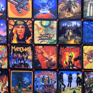 Könnte beinhalten: Eine Sammlung von zwanzig quadratischen Stoffaufnähern mit farbenfrohen Grafikdrucken von Heavy-Metal-Albumcovern, darunter King Diamond, Manowar, Mercyful Fate und Motorhead, jeweils mit schwarzem gesticktem Rand und detaillierten Motiven.
