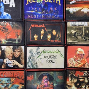 Op de afbeelding: Een verzameling rechthoekige patches met logo's van heavy metal bands en albumhoezen. Bands zijn onder meer Pantera, Megadeth, Metallica en Death. De patches zijn zwart met kleurrijke graphics en tekst.
