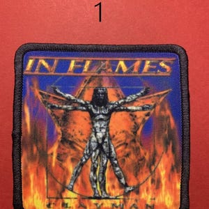 Peut inclure: &Eacute;cusson carr&eacute; avec le texte "IN FLAMES" au-dessus d'une figure de l'Homme de Vitruve dans une &eacute;toile, sur fond de flammes et de ciel bleu. L'&eacute;cusson a une bordure noire et le texte "CLAYMAN" en bas.