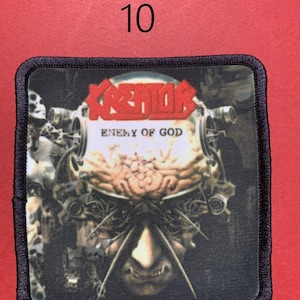 Peut inclure: &Eacute;cusson carr&eacute; avec le nom du groupe "KREATOR" en lettres rouges au-dessus du texte "ENEMY OF GOD". L'&eacute;cusson pr&eacute;sente un graphisme d&eacute;taill&eacute; d'un visage m&eacute;canique avec un cerveau et des composants m&eacute;talliques. L'&eacute;cusson a une bordure noire.