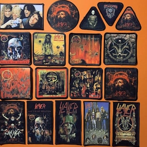 Könnte beinhalten: Eine Sammlung schwarzer Aufnäher mit verschiedenen Designs und dem Bandnamen "Slayer". Die Aufnäher zeigen Bilder von Schädeln, Bandmitgliedern und Albumcovern. Die Aufnäher haben verschiedene Formen, darunter Quadrate, Rechtecke und Dreiecke.