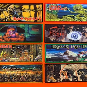 Könnte beinhalten: Acht rechteckige Stoffaufnäher mit Heavy-Metal-Band-Grafiken. Die Designs zeigen Illustrationen von Iron Maiden, Death und Slayer mit leuchtenden Farben, detaillierten Motiven und Bandlogos, die auf jedes Stück gedruckt sind, mit markanten Randnähten.