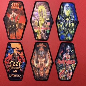 Puede incluir: Seis parches en forma de ataúd con logotipos y obras de arte de bandas de rock. Las bandas incluyen Ozzy Osbourne, Iron Maiden y Motörhead. Los parches tienen un borde negro y están sobre un fondo rojo.