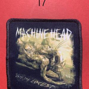 Peut inclure: &Eacute;cusson carr&eacute; noir avec un motif Machine Head. L'&eacute;cusson pr&eacute;sente le nom du groupe en blanc, une illustration d&eacute;taill&eacute;e et le texte "Unto the Locust". L'&eacute;cusson a une bordure noire et est pos&eacute; sur un fond rouge.
