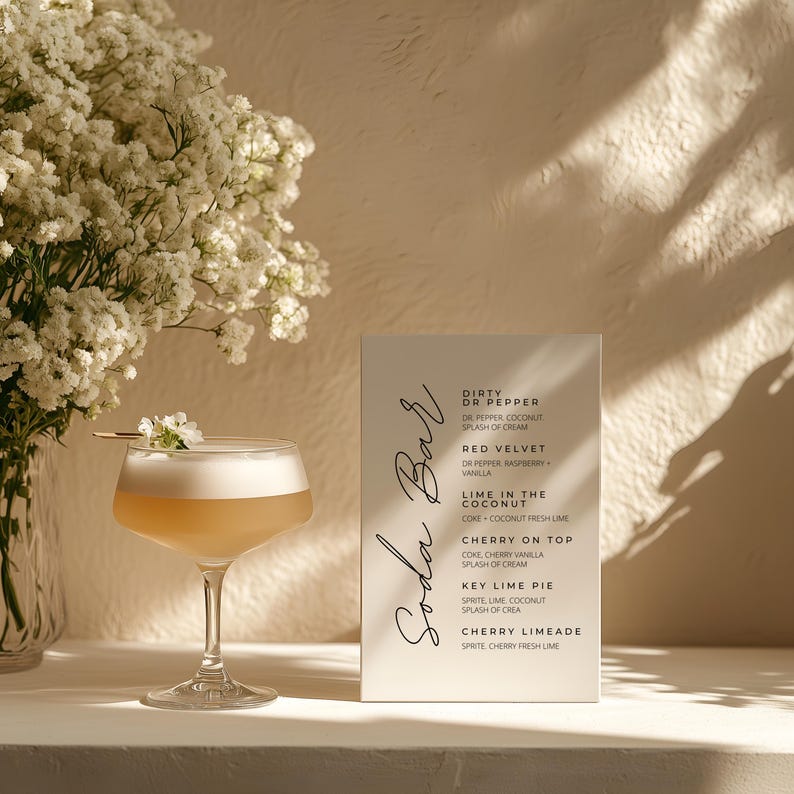 Op de afbeelding: Een cocktailglas met een lichtgekleurde drank en wit schuim, gegarneerd met een bloem, staat naast een menu met de tekst "Soda Bar". Het menu bevat verschillende recepten voor drankjes op basis van frisdrank. Een vaas met witte bloemen staat op de achtergrond.