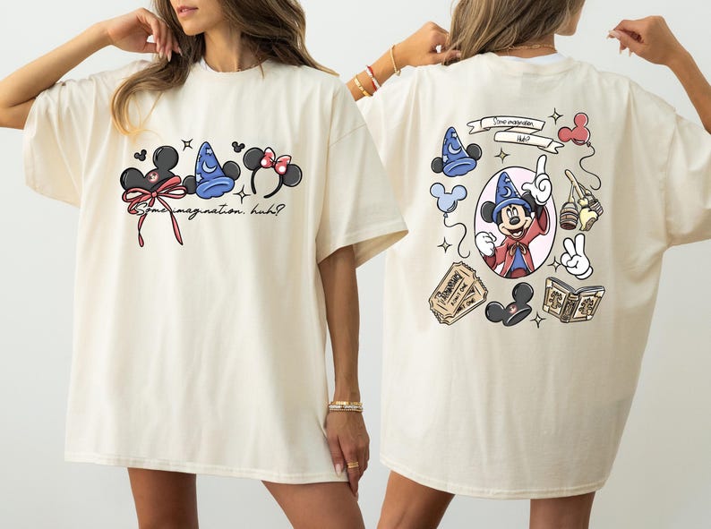 May include: Cream-colored t-shirt featuring Disney-themed graphics. The front displays Mickey Mouse ears, a sorcerer's hat, and text. The back showcases Mickey Mouse as a sorcerer, along with other Disney elements.