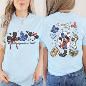 May include: Light blue t-shirt featuring a front graphic with Mickey Mouse ears, a wizard hat, and the text "Some imagination, huh?" The back of the shirt has a Mickey Mouse graphic with the text "Some imagination, huh?" and other Disney-themed illustrations.
