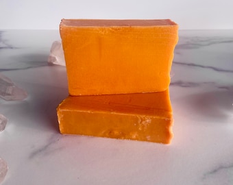 May include: Two bars of orange soap stacked on top of each other on a white marble surface.