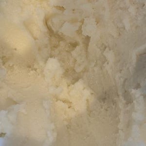 以下が含まれることがあります： わずかに黄色がかった、質感のあるオフホワイトの物質のクローズアップ。表面は粒状で不均一に見え、光と影の領域があります。全体的な質感は、クリーミーまたは固体の製品を示唆しています。