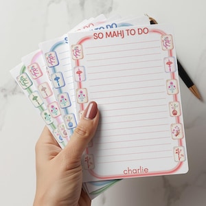 May include: A stack of colorful notepads with a Mahjong theme. Each notepad features a different pastel border and decorative Mahjong tile illustrations. The top notepad reads "SO MAHJ TO DO" and has the name "charlie" at the bottom.