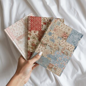 Op de afbeelding: Drie notitieboeken met harde kaft en patchwork bloemenpatronen in tinten rood, blauw, crème en roze. Op het bovenste notitieboek staat de naam HALEY in witte letters op een blauw bloemenpatroon gedrukt. Elk boek heeft een rechthoekige vorm.